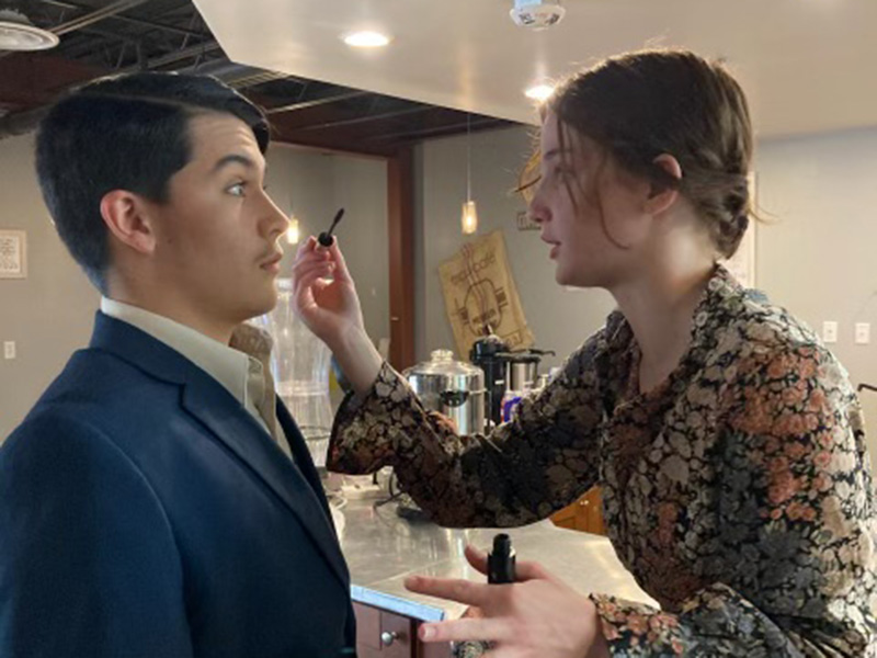Student putting mascara on a male student as theater makeup