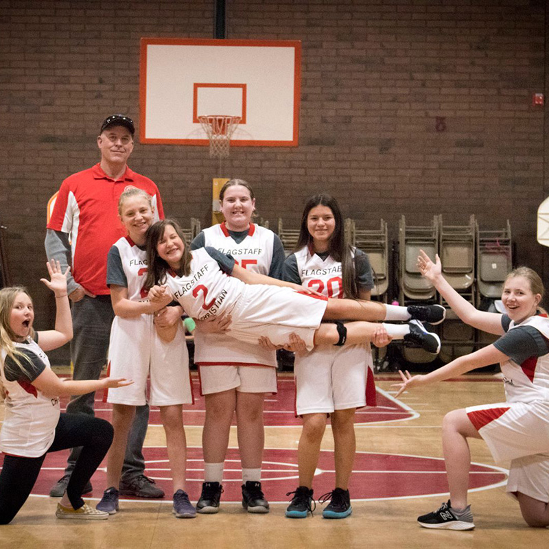 coach with the girls basketball team with a student stretching her legs, held by teammates