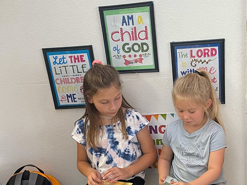 Two students reading in front of I am a child of God photos